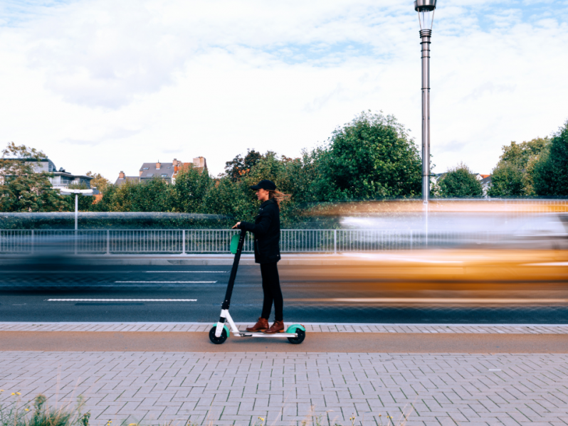 Eine Frau fährt mit einem e-Roller am Fahrradweg neben dem Gehsteig