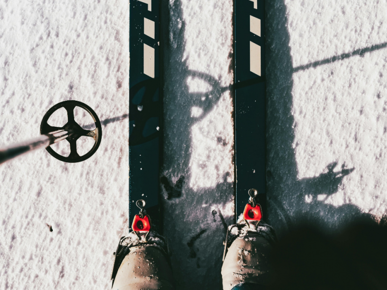 Eine Person steht mit schwarzen Skiern im Schnee und hält einen Skistock.